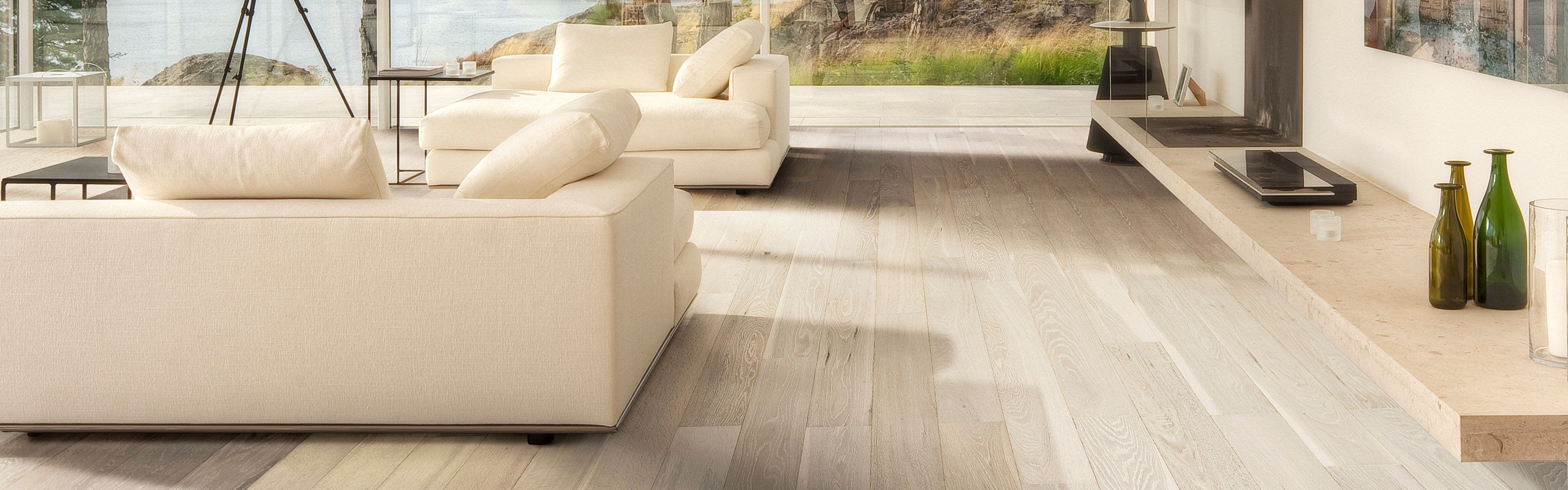 Stue med eikeparkett og lyse møbler.