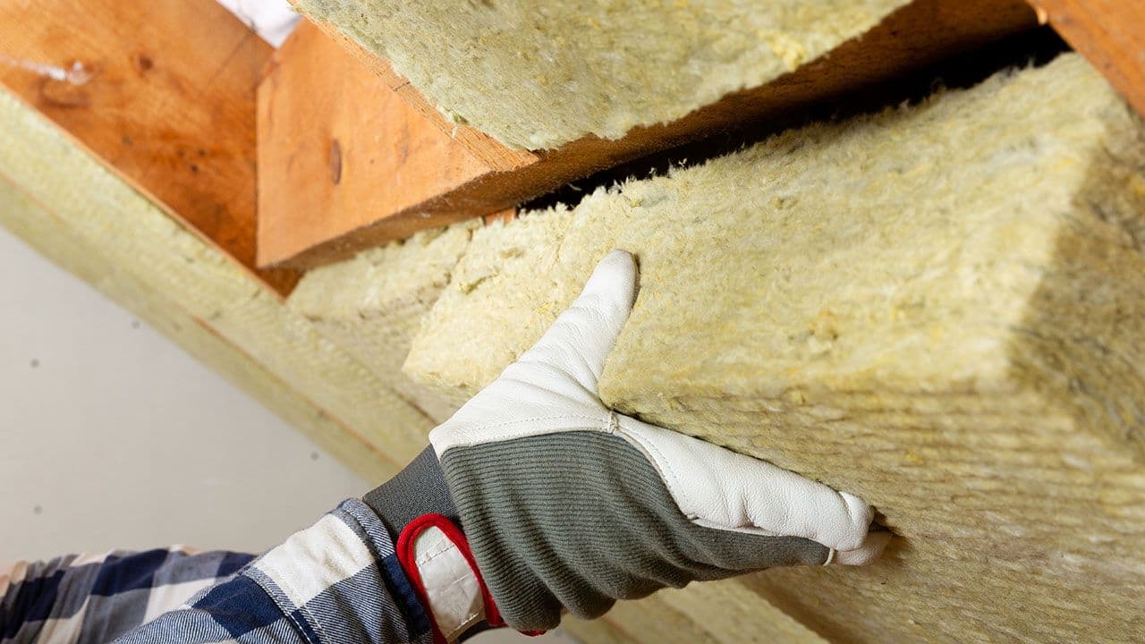 Hånd som dytter på plass isolasjon for å etterisolere loft.