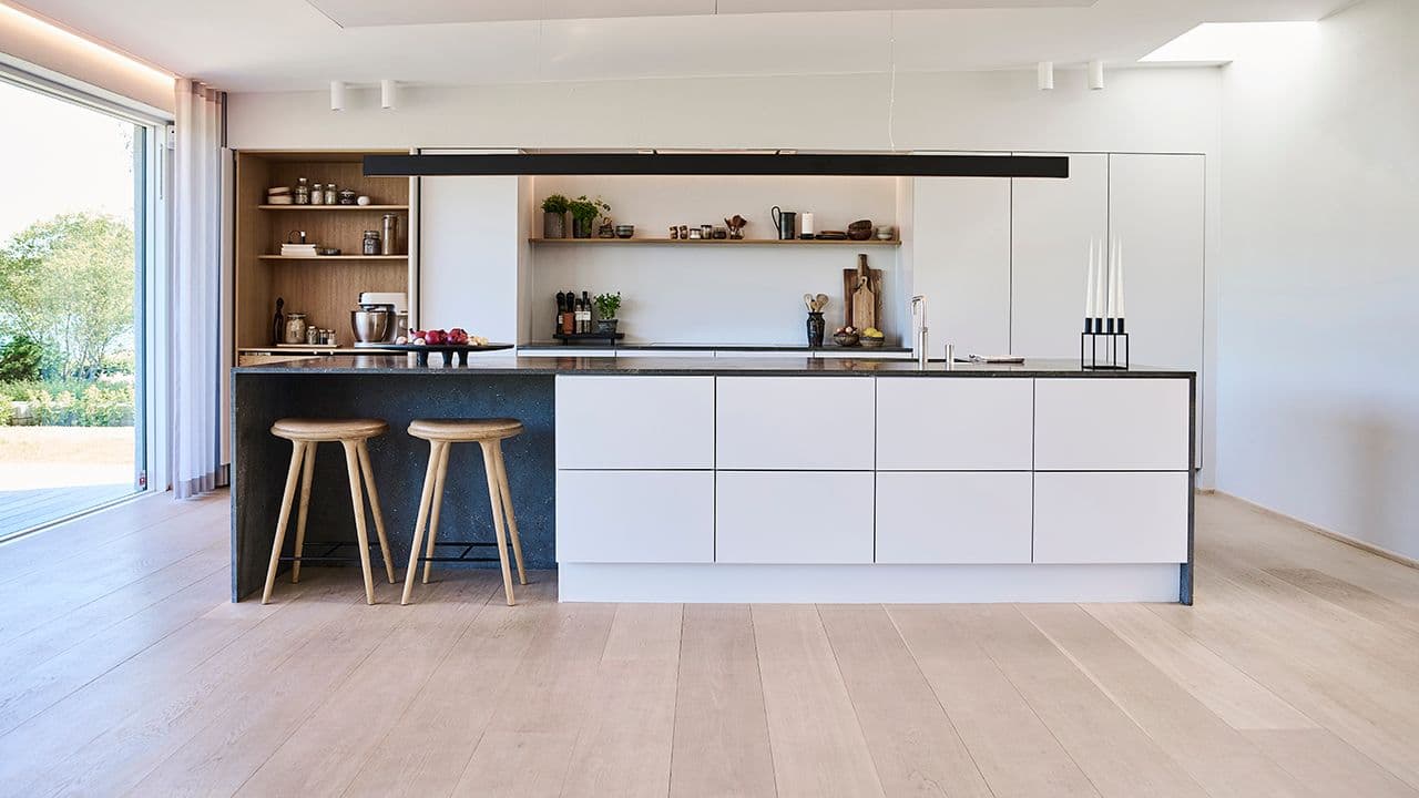 Typisk moderne kjøkken i hvitt med glatte fronter og mørk benkeplate i kompositt.