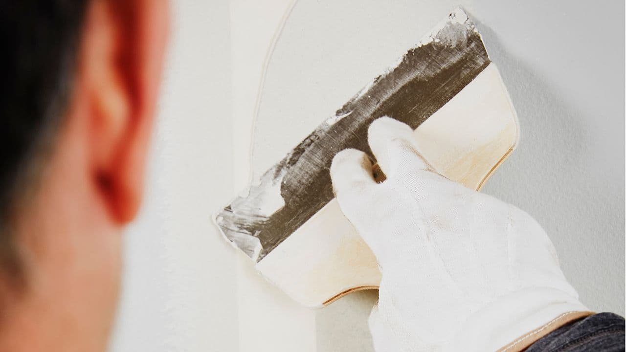 Nærbilde av mann som sparkler vegg før han skal male vegg inne.