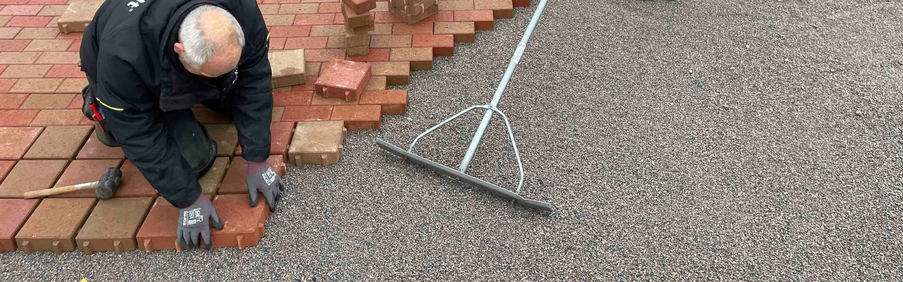 Mann som legger permeable belegningsstein med åpne fuger for drenering av hagen.