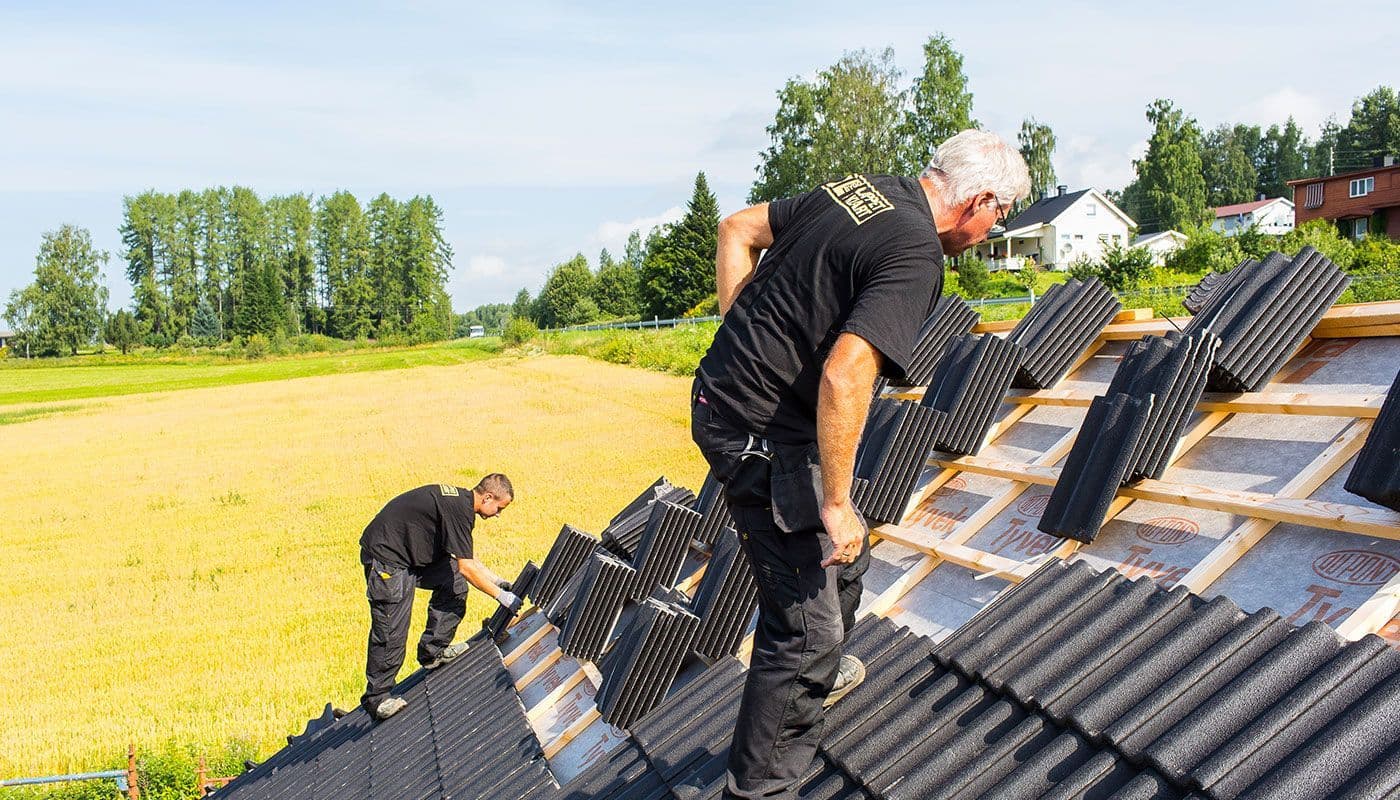 Menn som arbeider på taket med å legge takstein.