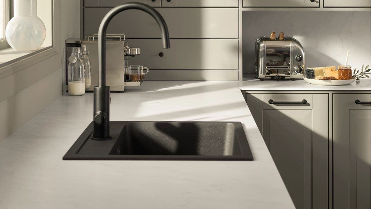 Hvit kompaktlaminat benkeplate på lysegrønt kjøkken med matt svart kjøkkenvask.