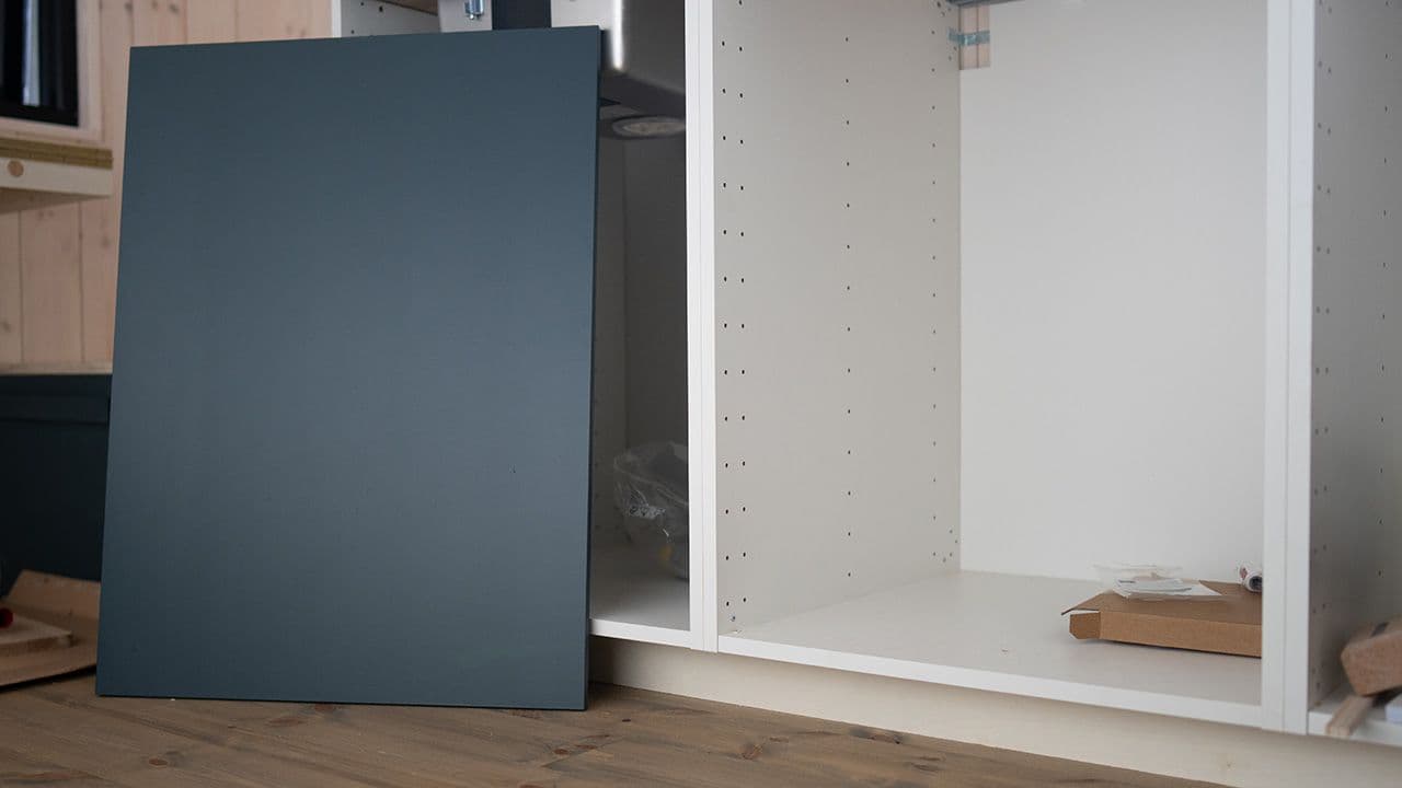 Kjøkkenfront som er malt blå som lener seg mot kjøkkenskap på sokkel i minihytte.