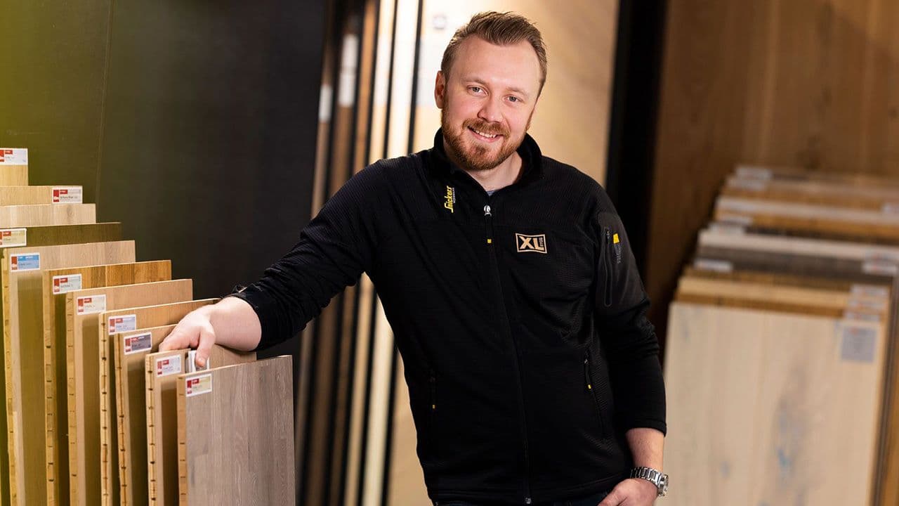 Mannlig XL-BYGG-ansatt som viser frem gulvprøver og forteller om sliping av parkettgulv.