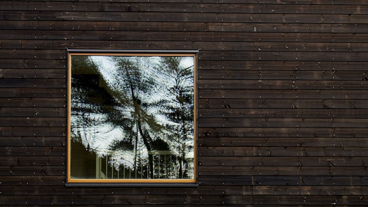 Hus med mørk kledning i tre og kvadratisk vindu.