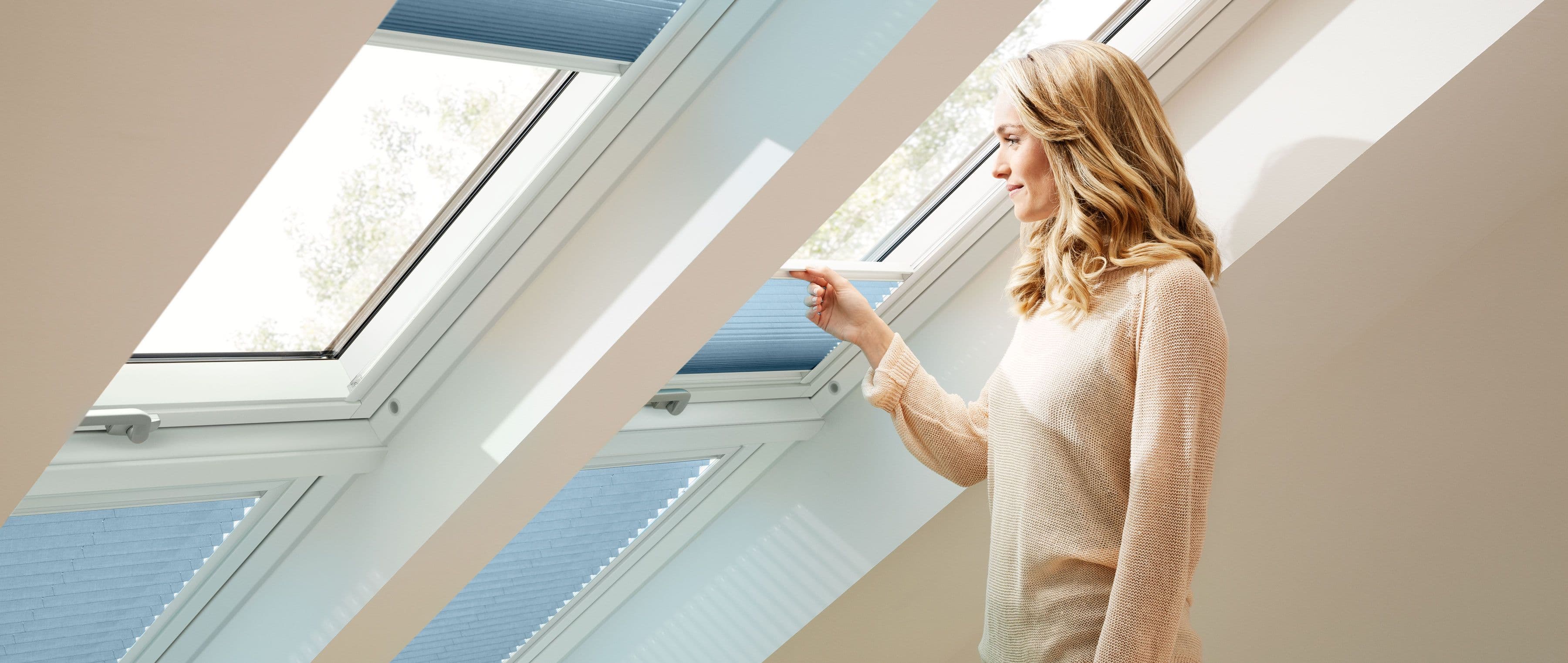 Kvinne ser ut av et takvindu som har plissegardin som solskjerming