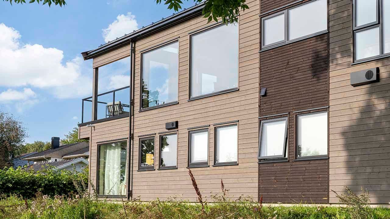 Hus med store vinduer og lys grå og mørkebrun kledning.