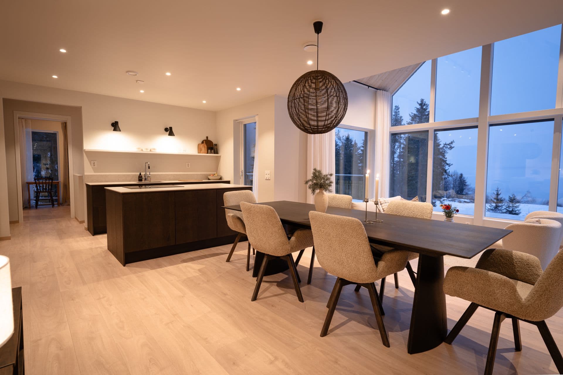 Åpen kjøkkenløsning med mørk eikekjøkken og spiseplass med spisebord i mørk eik og stoler med teddy-stoff.