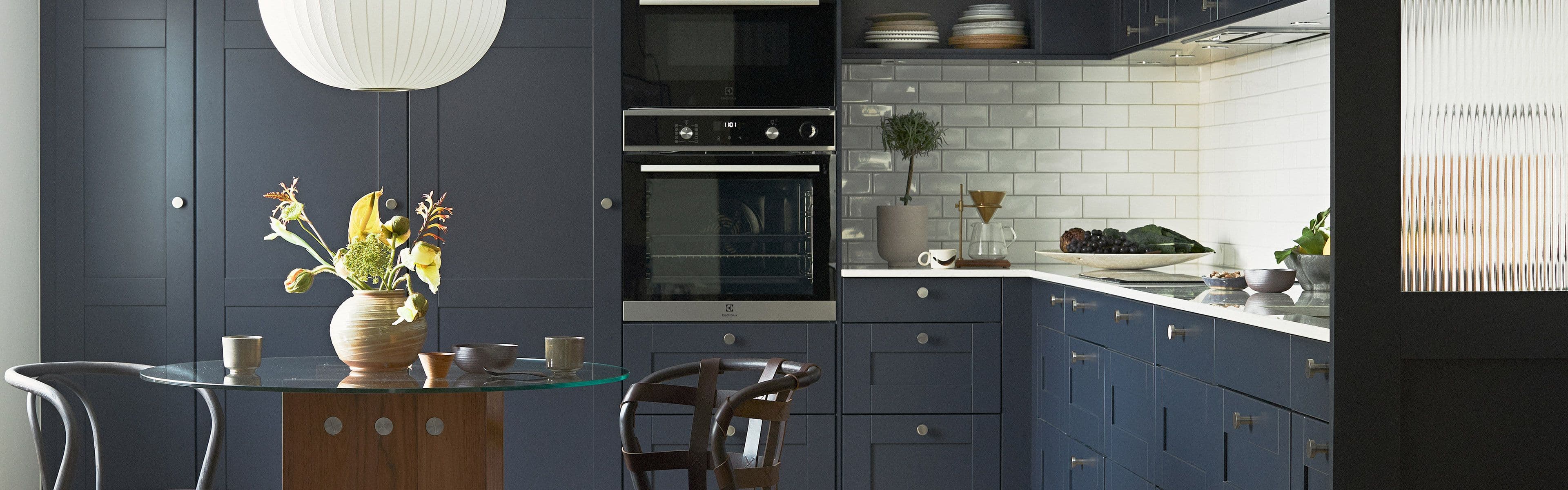 Blått kjøkken med over- og underskap og hvitevarer plassert i høyskap.