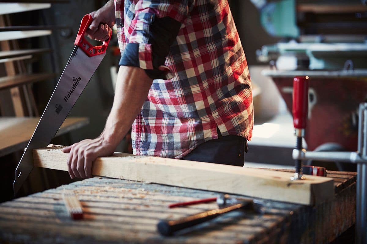 mann i rutete skjorte sager planke med en håndsag