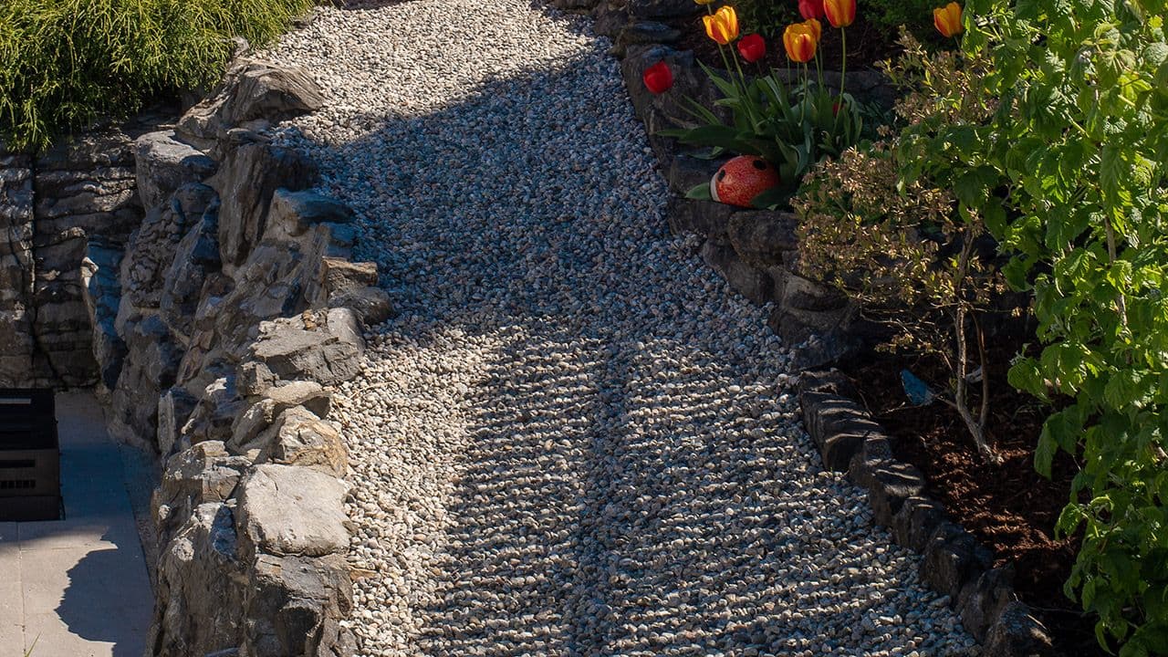 Stein rundt blomsterbed i hage med gangsti av dekorstein.