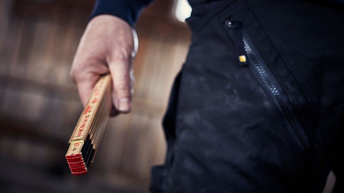 Mann i snekkerklær holder en meterstokk i hånden