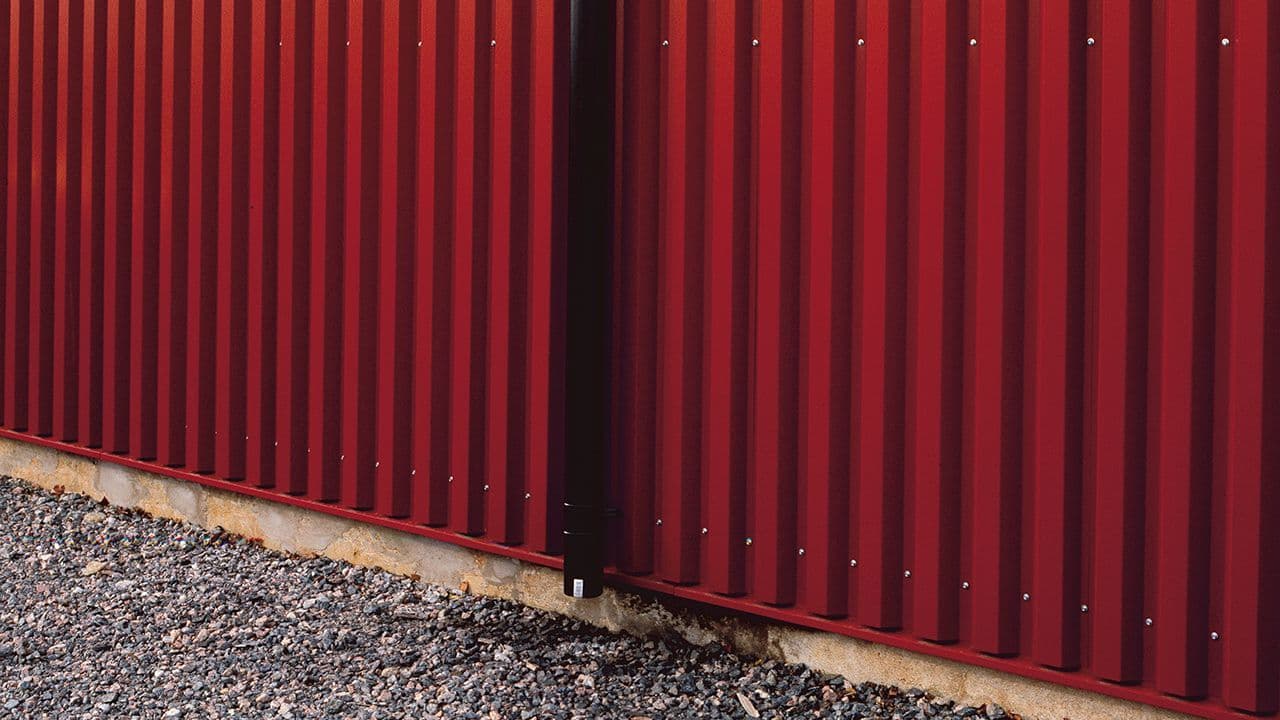 Nærbilde av sort takrenne på rød driftsbygning.