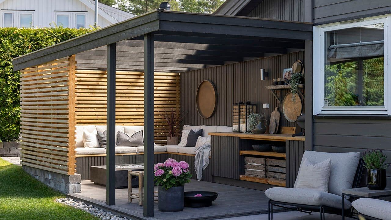 Utekjøkken i samme farge som huset med sittegruppe, levegger av spiler og tak.