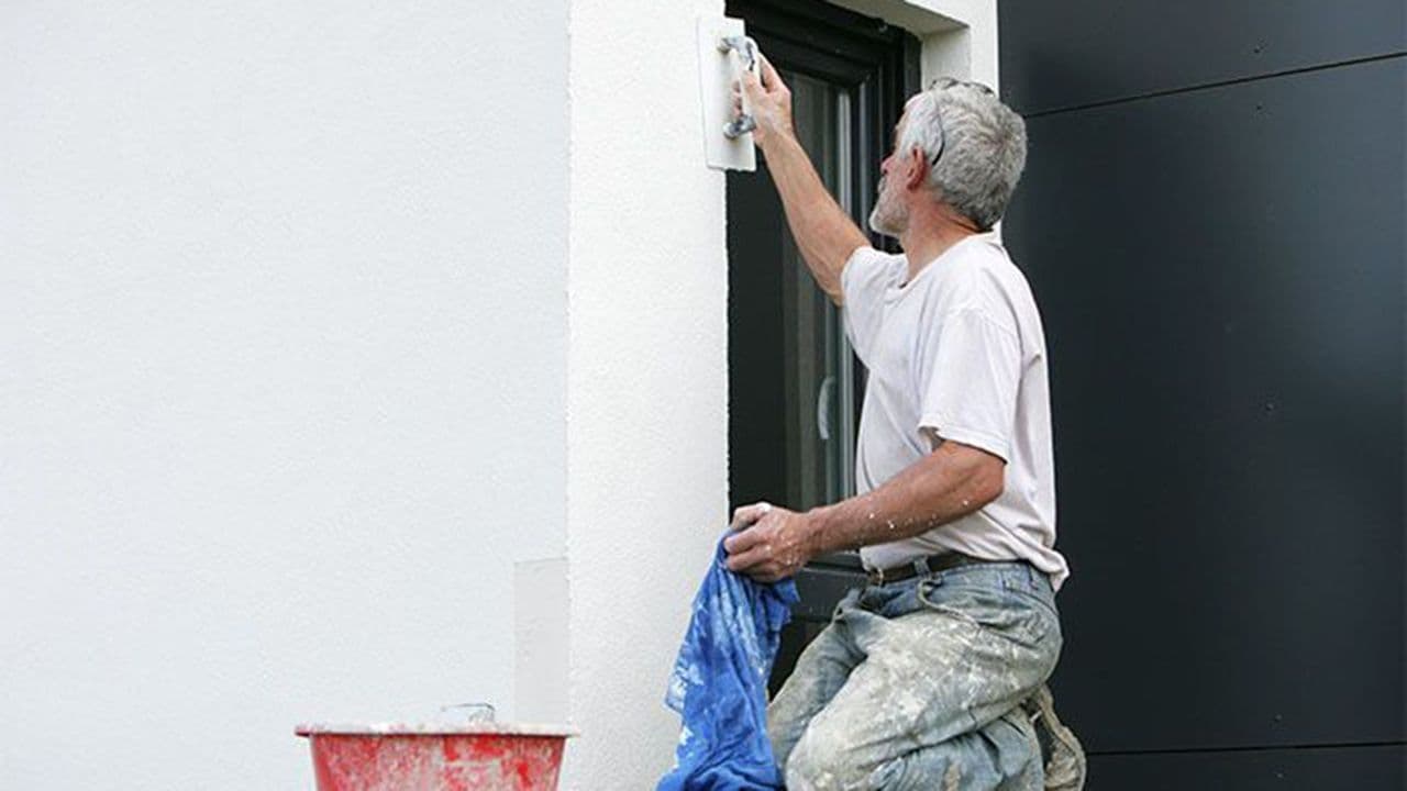 Håndverker som pusser fasade av mur.