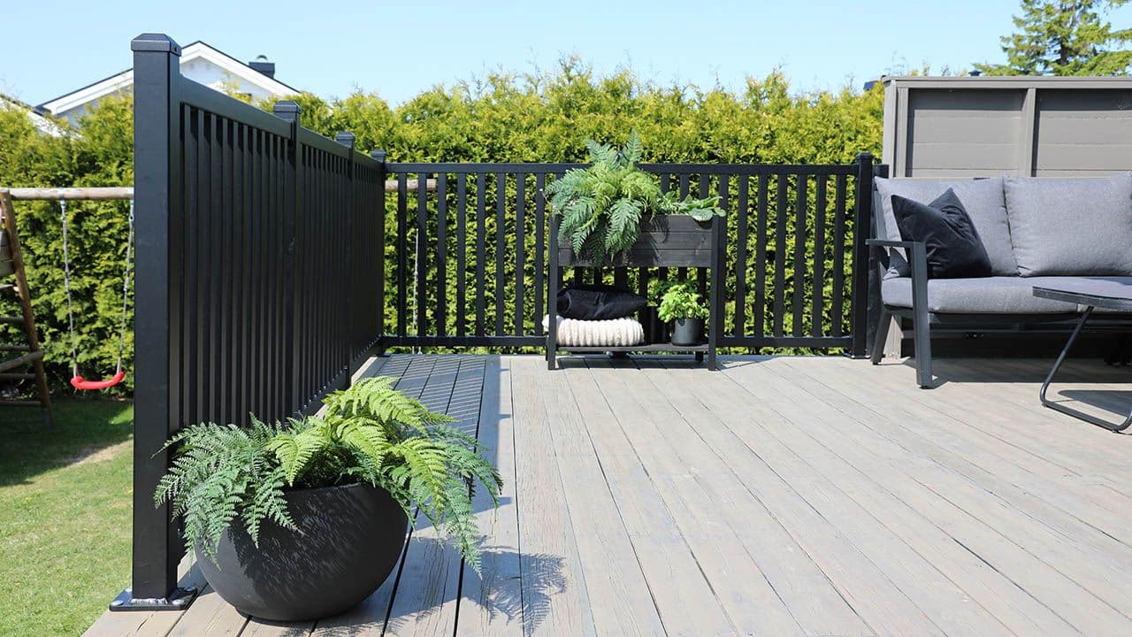 Svart rekkverk i aluminium på terrasse i hage.