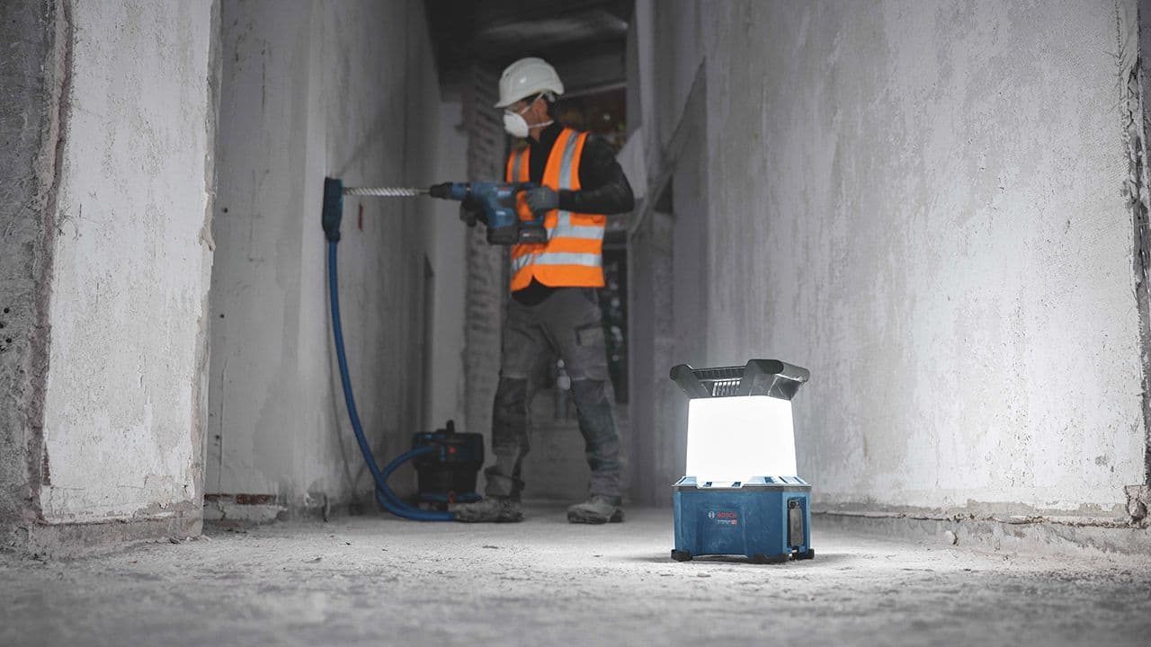 Arbeidslampe som lyser opp rom med betongvegger og håndverker som jobber.