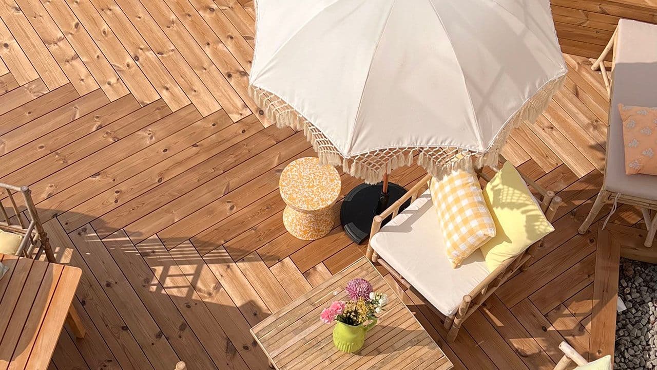 Terrasse med sittegruppe, parasoll og termofuru terrassebord som er lagt i fiskebensmønster.