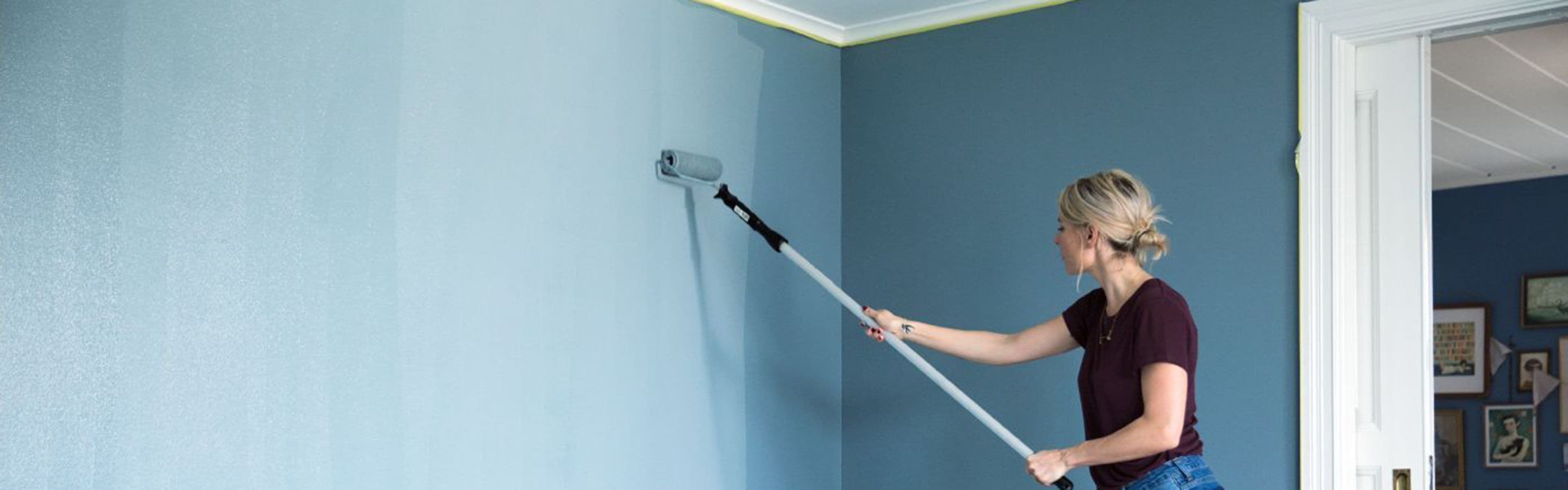 Kvinne maler vegg med malingsrulle og skaft.