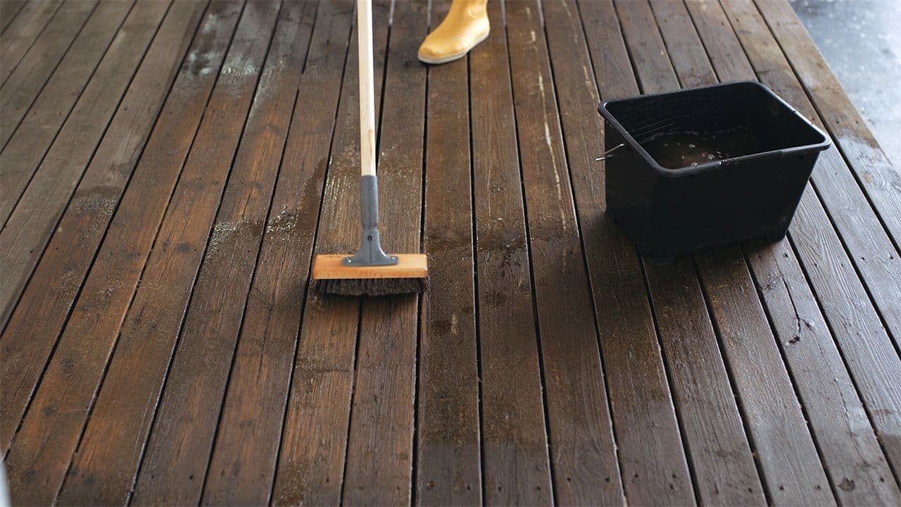 Kvinne som holder på å vaske terrasse med vann og kost.