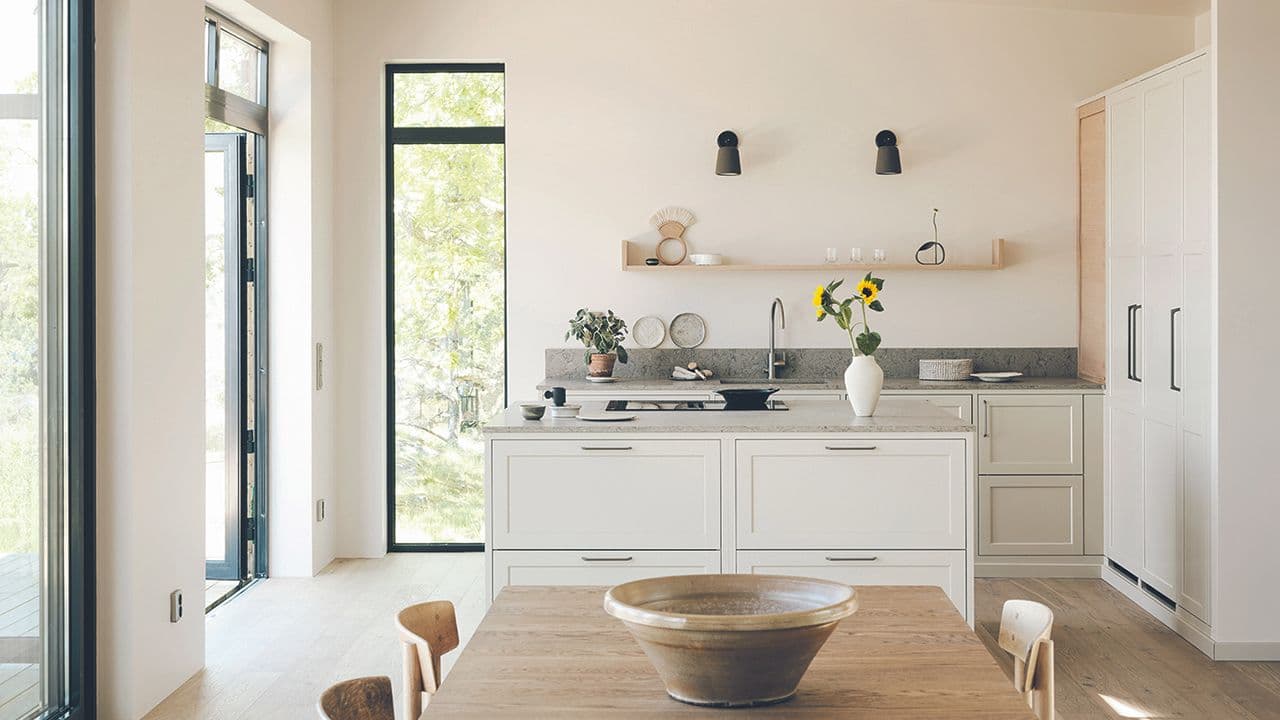 Lyst hyttekjøkken med kjøkkenøy i tilknytning til terrasse.