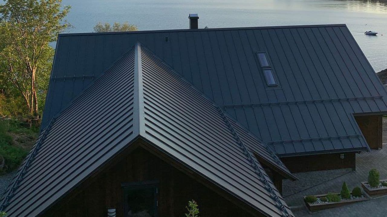 Sorte takplater fra Plannja på et hus som ligger flott til nede ved sjøen.